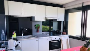 Eine moderne Küche mit weißen Schränken, einem eingebauten Ofen und einem großen Fenster mit Blick auf Grünflächen.
