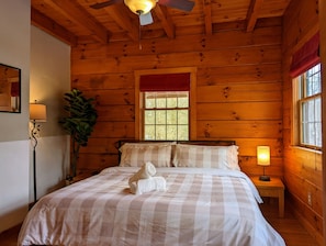 Quarto de cabana de madeira com cama, mesa de cabeceira, abajur e janela.