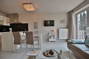Una sala de estar moderna con comedor, cocina y un amplio ventanal con vista a árboles.