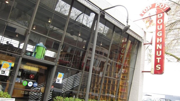 A storefront with a large glass window, a sign for 'Top Pot Doughnuts', and outdoor seating with metal chairs. - Charming Belltown Corner Studio (Seattle)