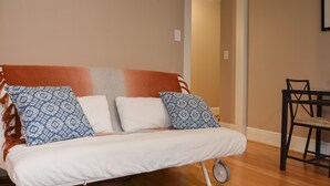 A small, cozy room with a sofa, two patterned pillows, a small table, and a chair. - Charming Belltown Corner Studio (Seattle)
