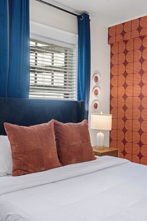 A hotel room with a bed, blue curtains, a patterned wall, a bedside lamp, and a window with blinds. - Charming Studio - Downtown Seattle - 98 Walk Score (Seattle)