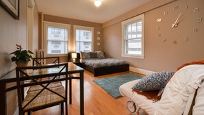 A bedroom with a bed, a desk, a chair, a clock, and a window. - Charming Belltown Corner Studio (Seattle)
