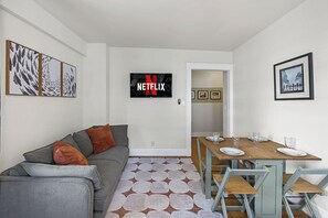 A modern living room with a grey sofa, a wooden dining table with chairs, a flat-screen TV, and a patterned rug. - Charming Studio - Downtown Seattle - 98 Walk Score (Seattle)
