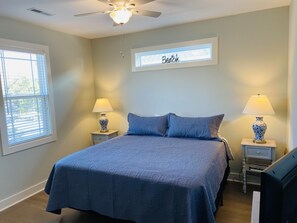 Quarto com uma cama, duas mesas de cabeceira com luminárias, um ventilador de teto e uma janela com persianas.