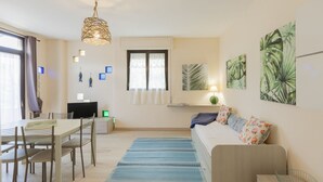 A modern living room with a sofa, a dining table with chairs, a TV, and artwork on the walls.