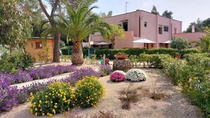 Ein Garten mit verschiedenen blühenden Pflanzen und einem Gebäude mit einer rosafarbenen Fassade.