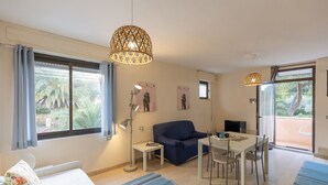 Ein modernes Zimmer mit einem Bett, einem Sofa, einem Esstisch mit Stühlen, einer Lampe und einem großen Fenster mit Vorhängen.