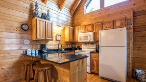 A wooden cabin-style kitchen with a central island, wooden stools, a refrigerator, and a microwave. - Bearadise City🐻 Loft Cabin w/ Mtn Views, Hot Tub, & Pool Table! (Pigeon Forge)