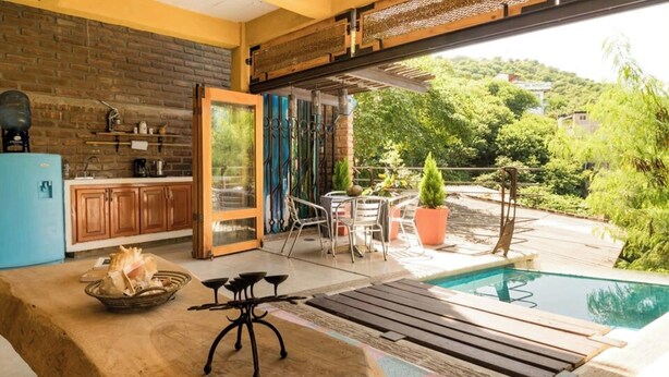 A modern kitchen with wooden cabinets, a blue refrigerator, and a dining area with a poolside view.