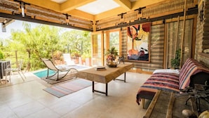 A spacious indoor area with a pool, a wooden table, a sofa, and a large window with a view of greenery.