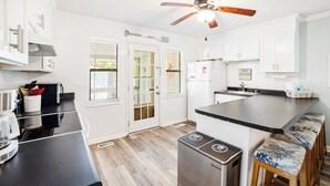 A modern kitchen with white cabinets, a black countertop, a stainless steel refrigerator, and a ceiling fan. - The Inkwell ~ An Oak Island Gem (Oak Island)
