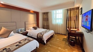 Ein Hotelzimmer mit zwei Betten, einem Schreibtisch, einem Fernseher und einem fenster mit Vorhängen.