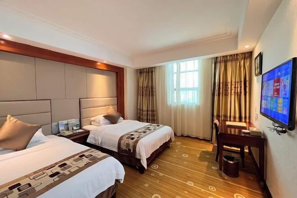 A hotel room with two beds, a desk, a TV, and a window with curtains.