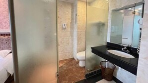 Ein Badezimmer mit Duschkabine aus Glas, einer weißen Toilette, einem schwarzen Waschbecken und einem Spiegel sowie einem Marmorboden.
