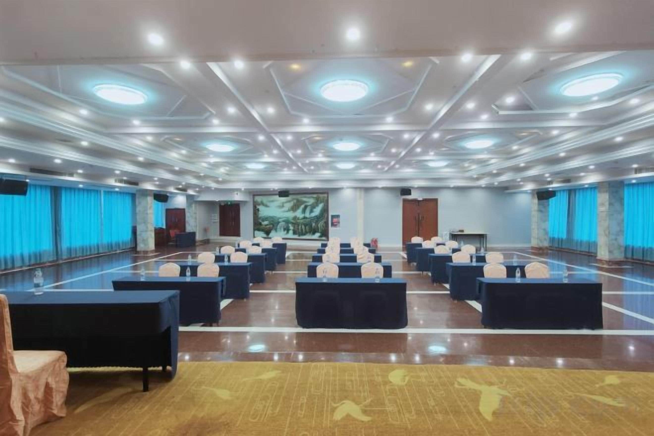 A large conference room with rows of tables and chairs, a stage, and a large screen.