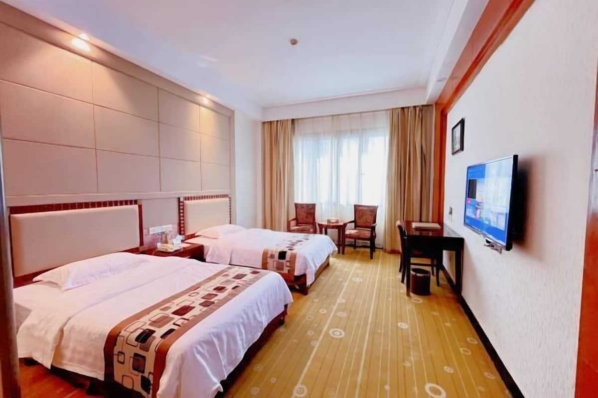A hotel room with two beds, a television, a small table, and a chair.