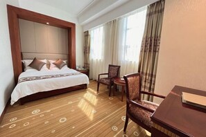 A hotel room with a large bed, a wooden headboard, a dining table, and a chair. - Huaxi International Hotel (Baise)