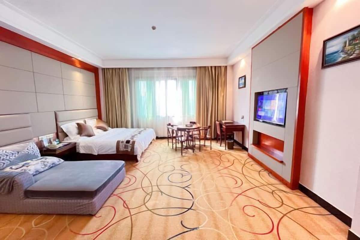 A hotel room with two beds, a sofa, a dining table, chairs, a TV, and a large window with curtains.