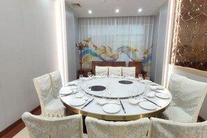 A round dining table set for six with white chairs, a mural on the wall, and a decorative wall panel.