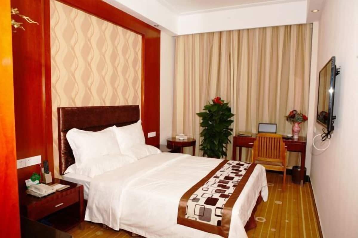 A hotel room with a bed, a desk, a chair, a plant, and a TV.
