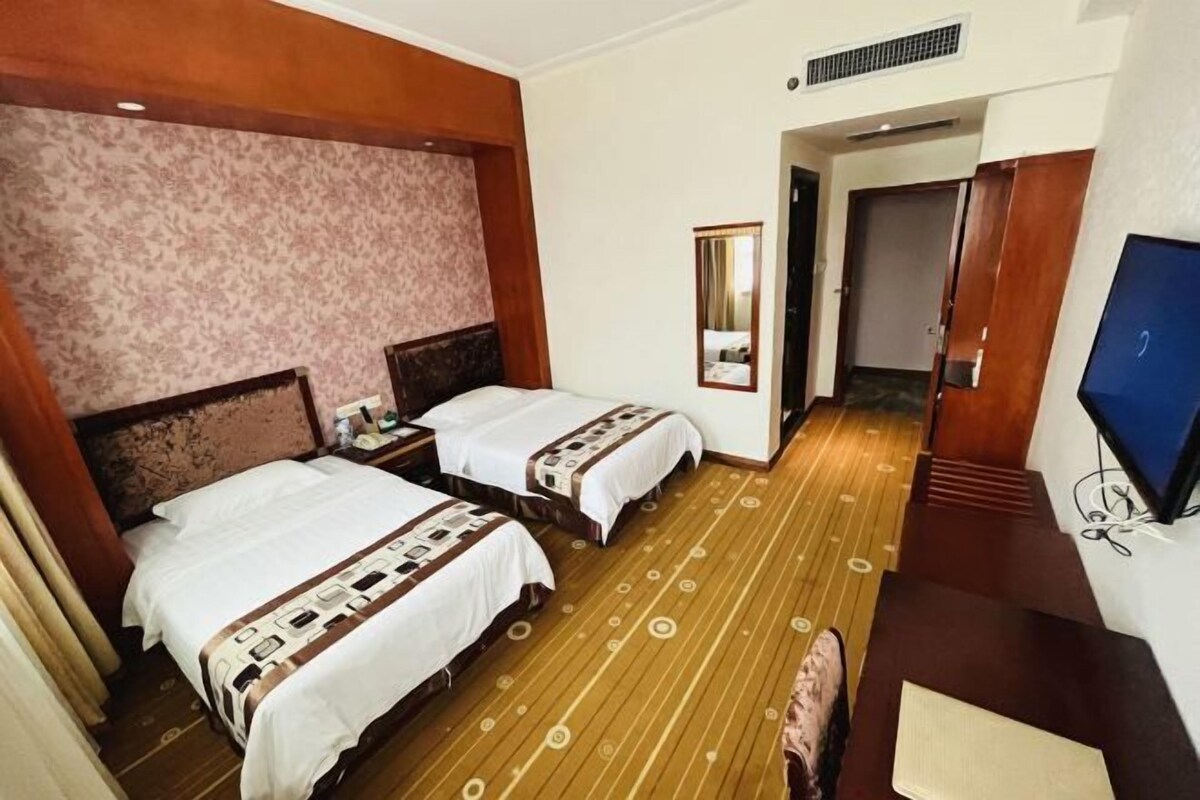 A hotel room with two beds, a wooden floor, a television, and a mirror.