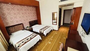 A hotel room with two beds, a wooden floor, a television, and a mirror.