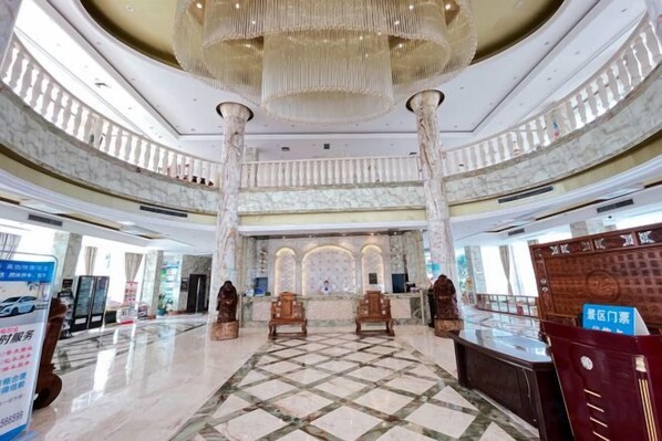 A spacious lobby with a marble floor, large chandeliers, and a reception desk.