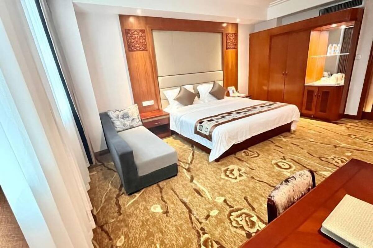 A hotel room with a large bed, a sofa, a desk, and a wardrobe.