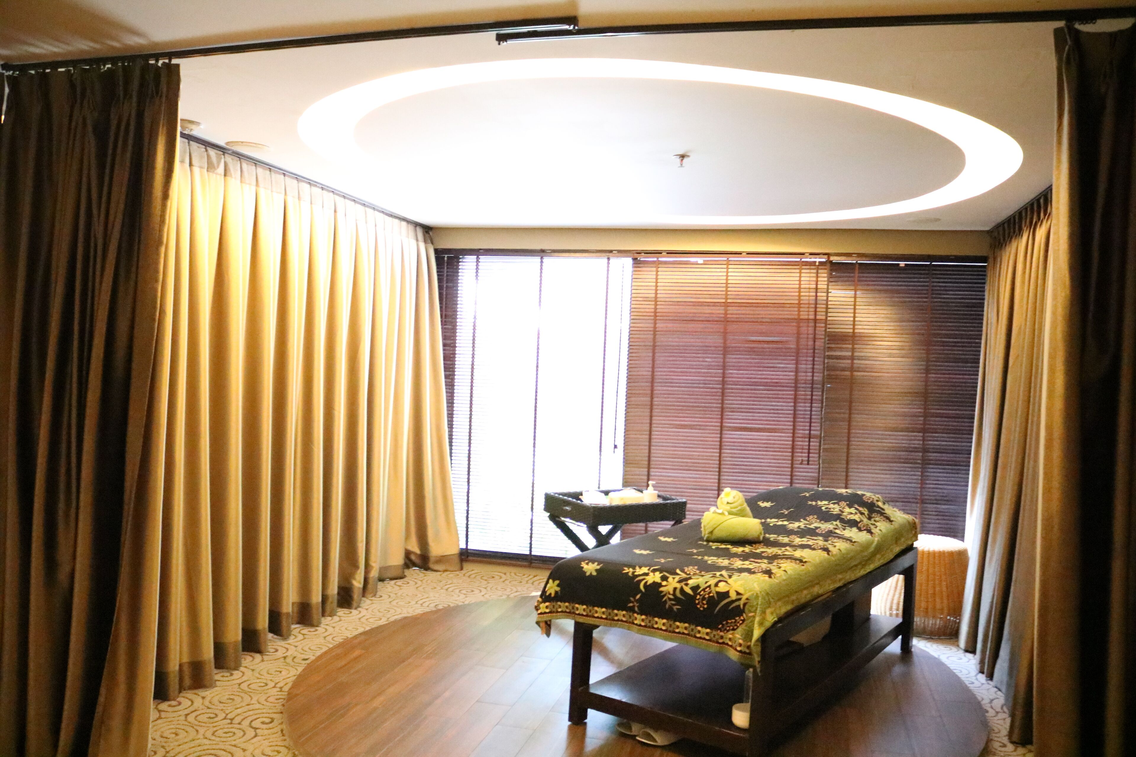 A hotel room with a bed, a small table, and a window with blinds.