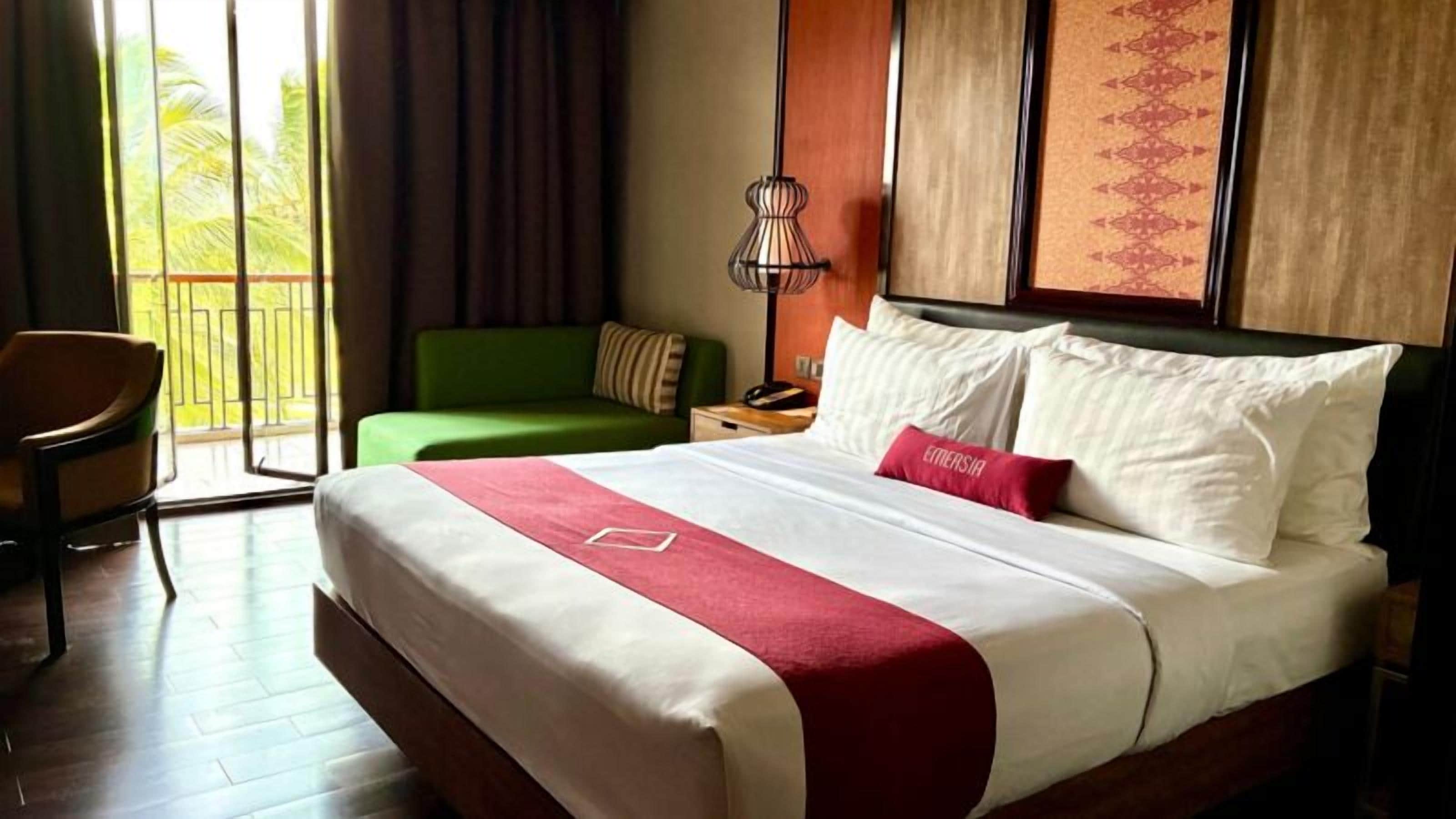A hotel room with a bed, a green sofa, a chair, a nightstand, and a lamp.