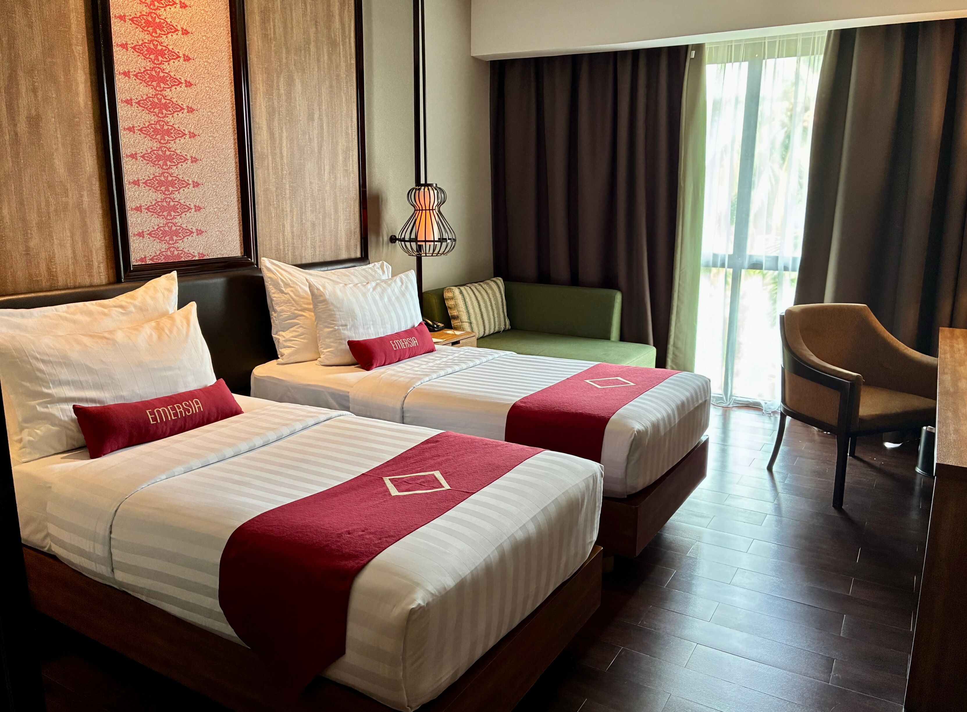 A hotel room with two beds, a green sofa, a chair, and a view of the outdoors.