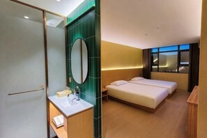 Une chambre d’hôtel comprenant un lit, une table de chevet, un miroir, une fenêtre donnant sur la ville et une salle de bain avec un lavabo et un miroir.