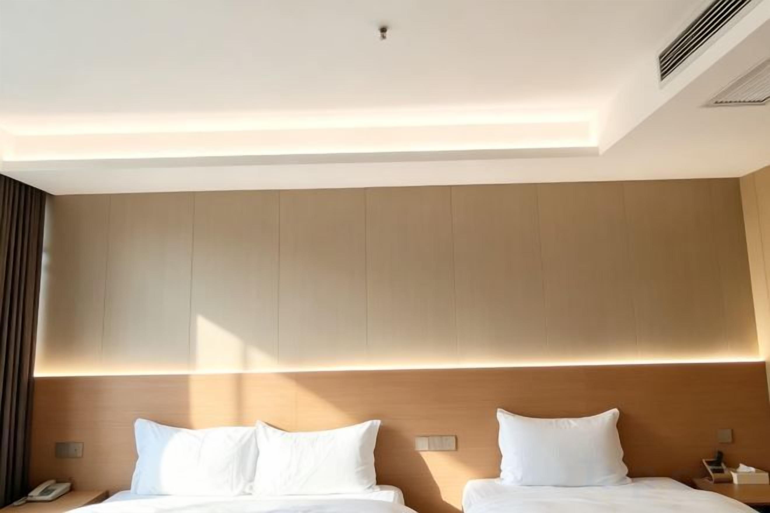 Habitación de hotel con dos camas, cabecera de madera, mesita de noche con lámpara y teléfono a la izquierda.