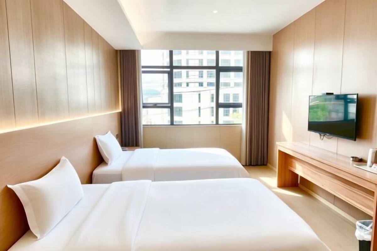 Hotellihuone, jossa on kaksi sänkyä, televisio ja suuri ikkuna.