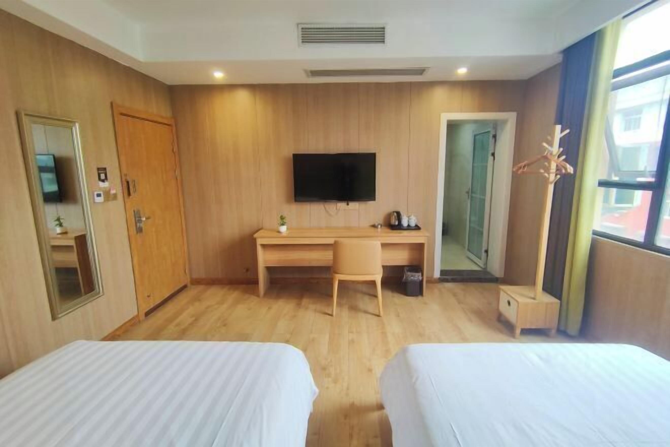 Ein Hotelzimmer mit zwei Betten, einem Schreibtisch, einem Fernseher und einem Fenster mit Vorhängen.