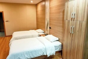 Een hotelkamer met twee bedden, een houten garderobe en een effen muur.