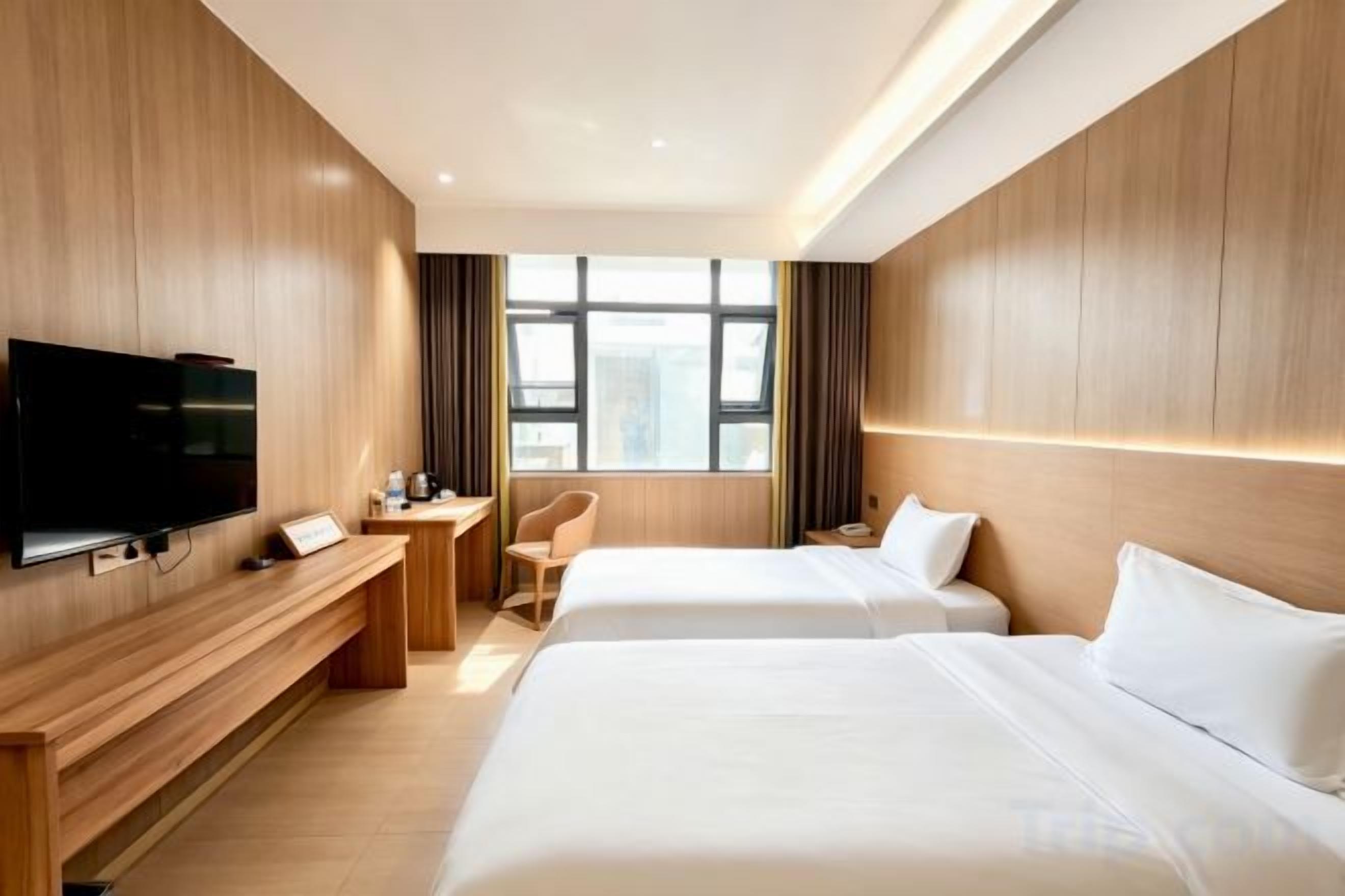A hotel room with two beds, a desk, a chair, a TV, and a window with curtains.