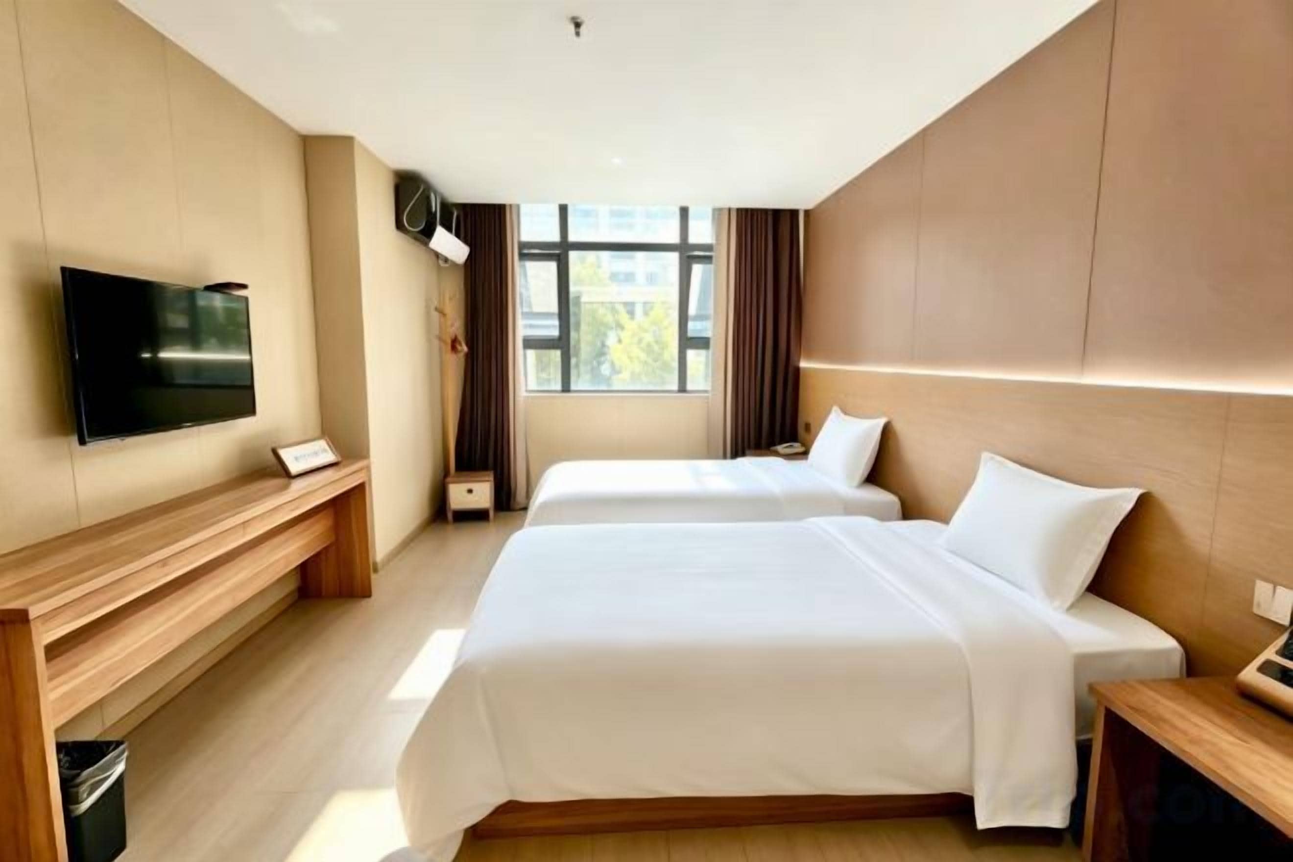 A hotel room with two beds, a TV, a desk, and a window with curtains.