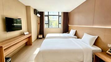 Habitación de hotel con dos camas, televisión, escritorio y ventana con cortinas.