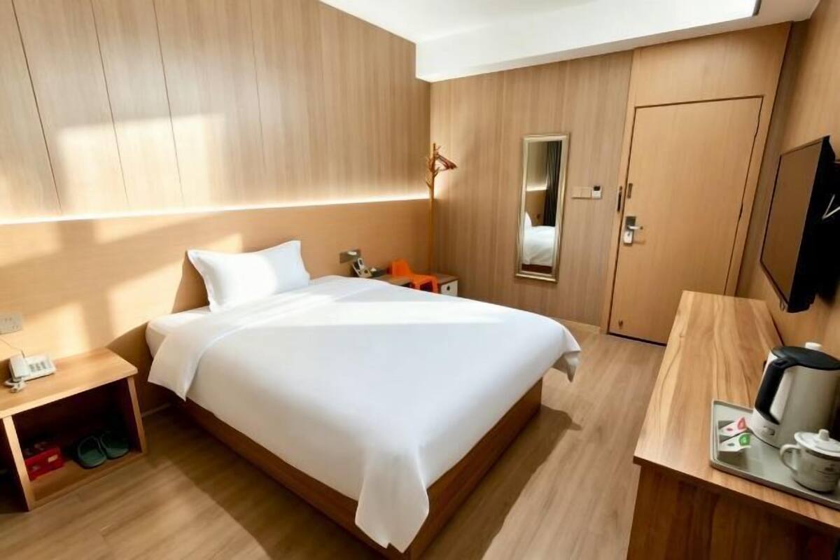 Hotellihuone, jossa on sänky, yöpöytä, peili, vaatekaappi ja työpöytä sekä kahvinkeitin.