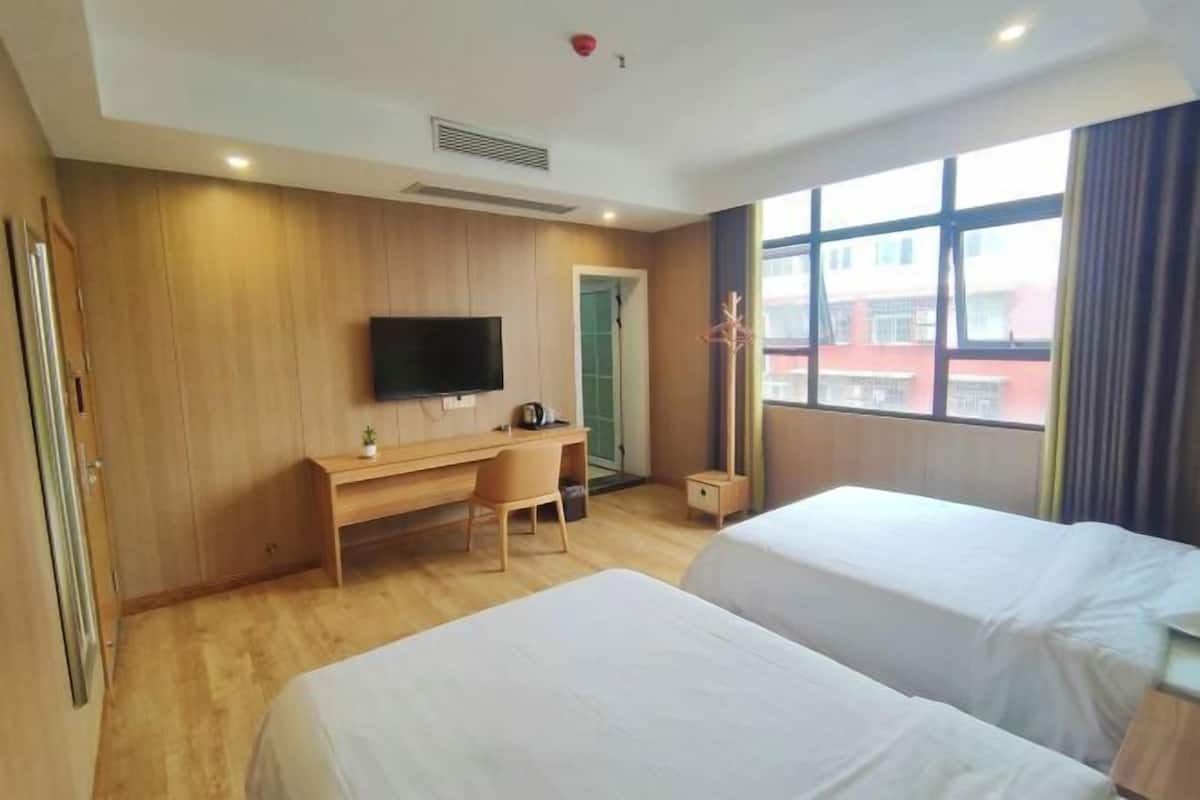 Hotellihuone, jossa on kaksi sänkyä, työpöytä, tuoli, televisio ja ikkuna, josta on näkymä rakennuksiin.