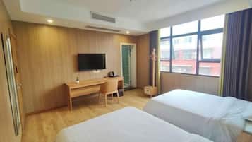 A hotel room with two beds, a desk, a chair, a TV, and a window with a view of buildings.