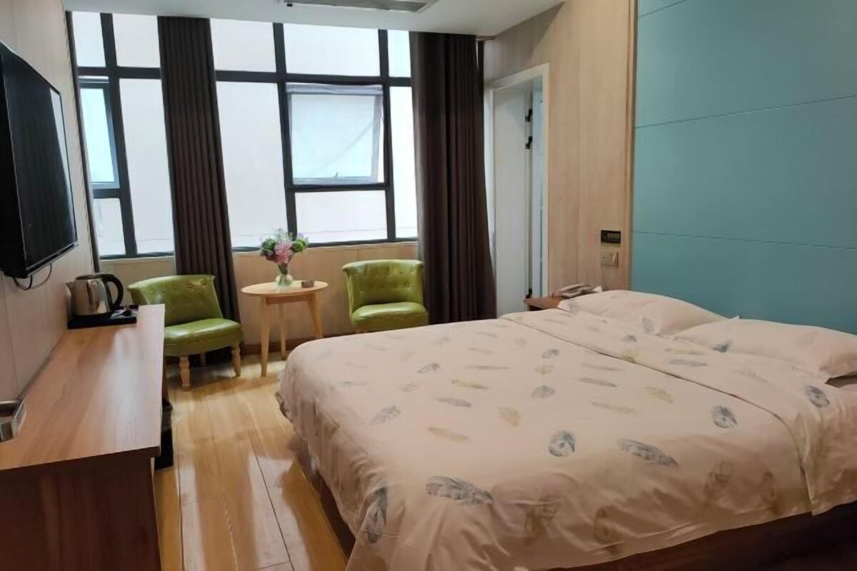 Een hotelkamer met een bed, een bureau, een stoel, een klein tafeltje met een vaas en een raam met gordijnen.