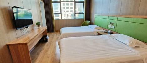A hotel room with two beds, a TV on a wooden console, a window with a city view, and a green headboard.