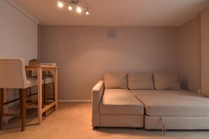 A bedroom with a sofa bed, a wooden chair, and a small table with a plant.
