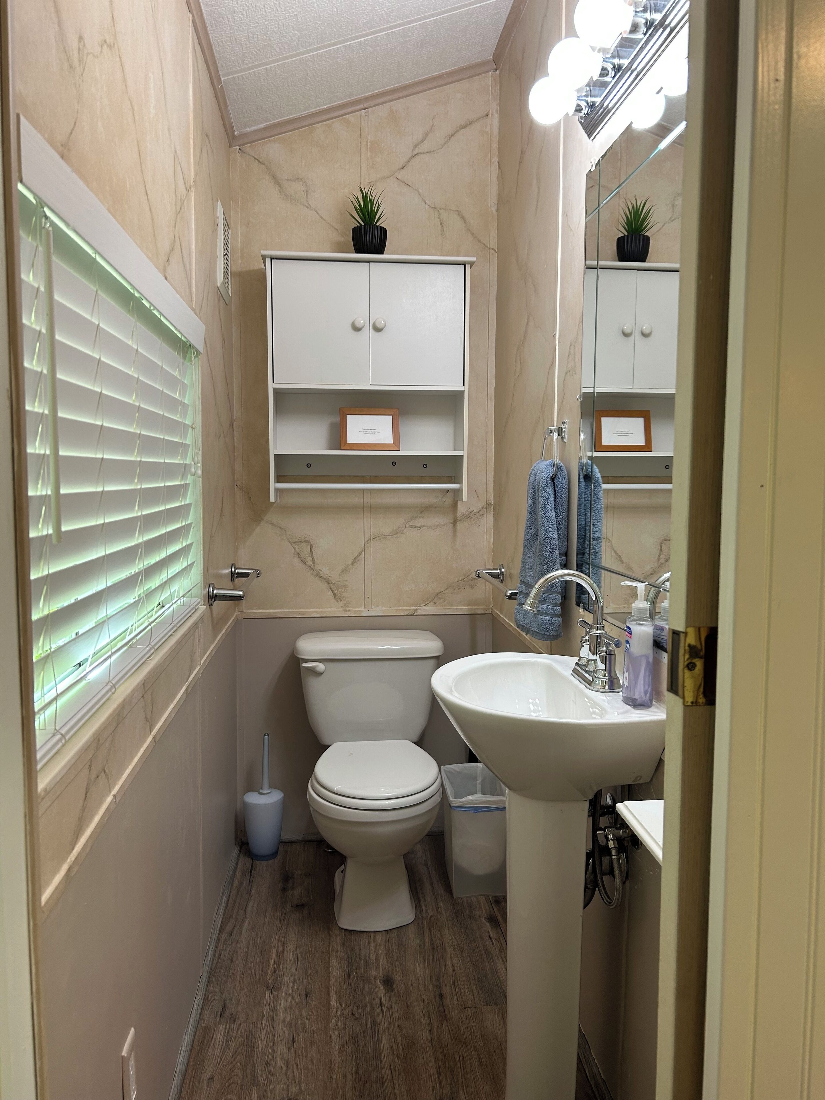 Baño compacto con inodoro, lavabo y tocador, que presenta paredes de mármol y suelo de madera.