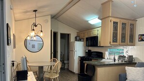 A compact kitchen with wooden cabinets, a central island, and a dining area with chairs. - Point Sebago 3 BR, 1.5 bath Maine lake cottage near beach on Purple Rd (Casco)