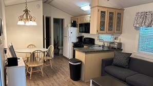 A compact kitchen with wooden cabinets, a refrigerator, a stove, and a sink. There is a dining area with a table and chairs, and a small seating area with a sofa and a coffee table. - Point Sebago 3 BR, 1.5 bath Maine lake cottage near beach on Purple Rd (Casco)