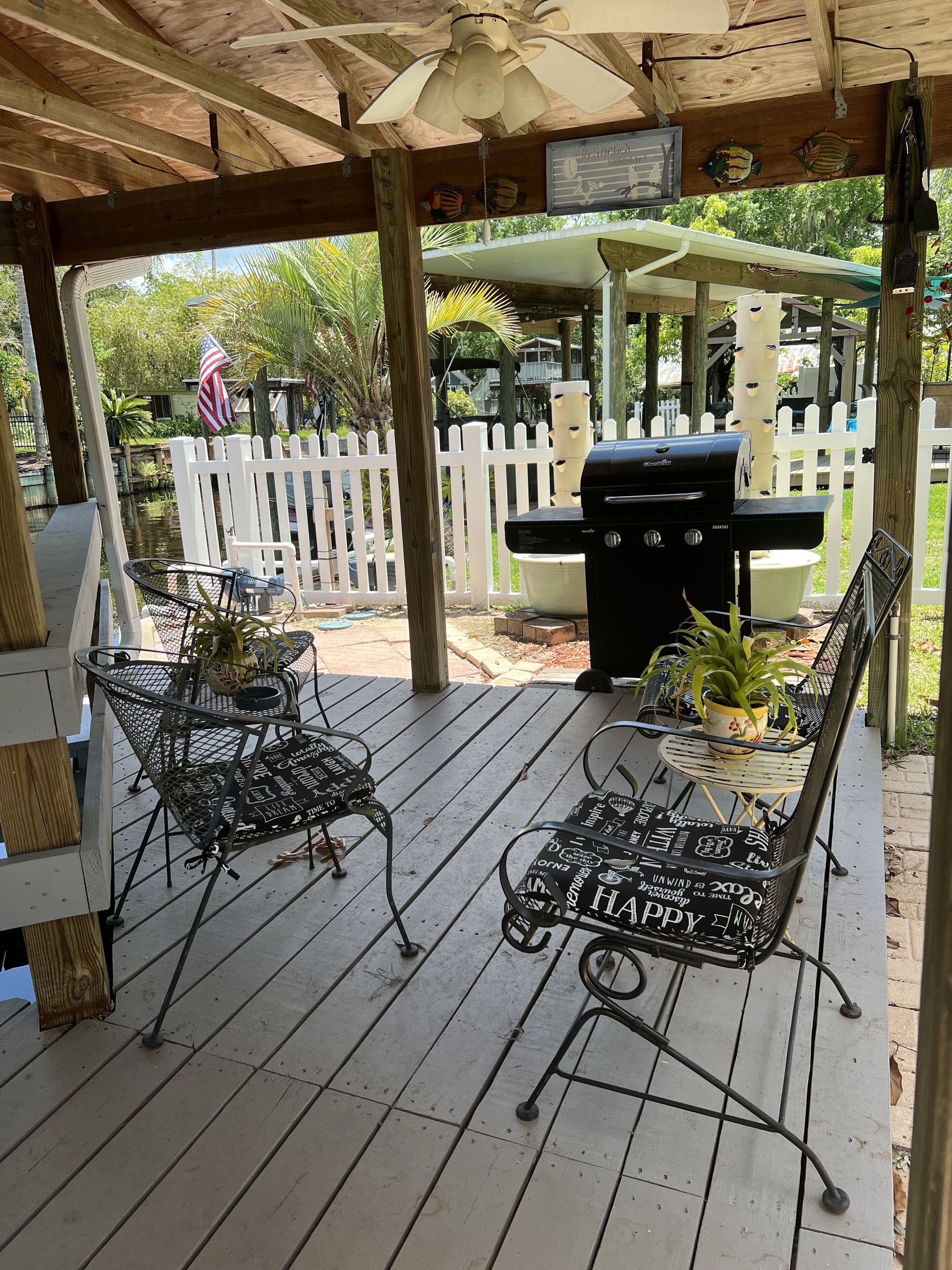 A covered patio with a grill, metal chairs, and a table.